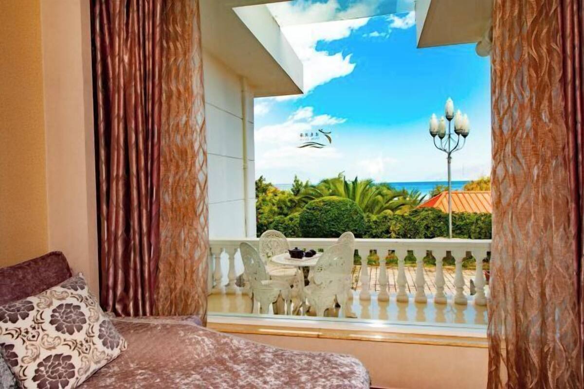 A room with a bed, a balcony with a view of the sea, and a table with chairs.