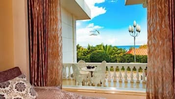 A room with a bed, a balcony with a view of the sea, and a table with chairs.