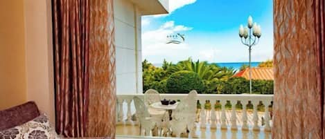 A room with a bed, a balcony with a view of the sea, and a table with chairs.