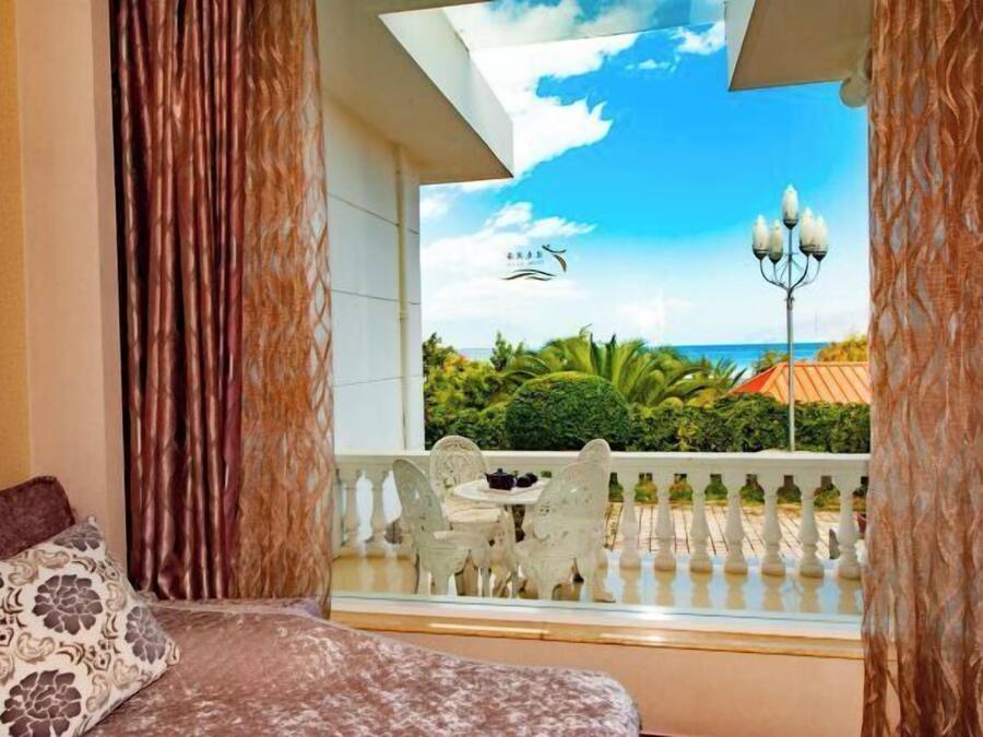 A room with a bed, a balcony with a view of the sea, and a table with chairs.