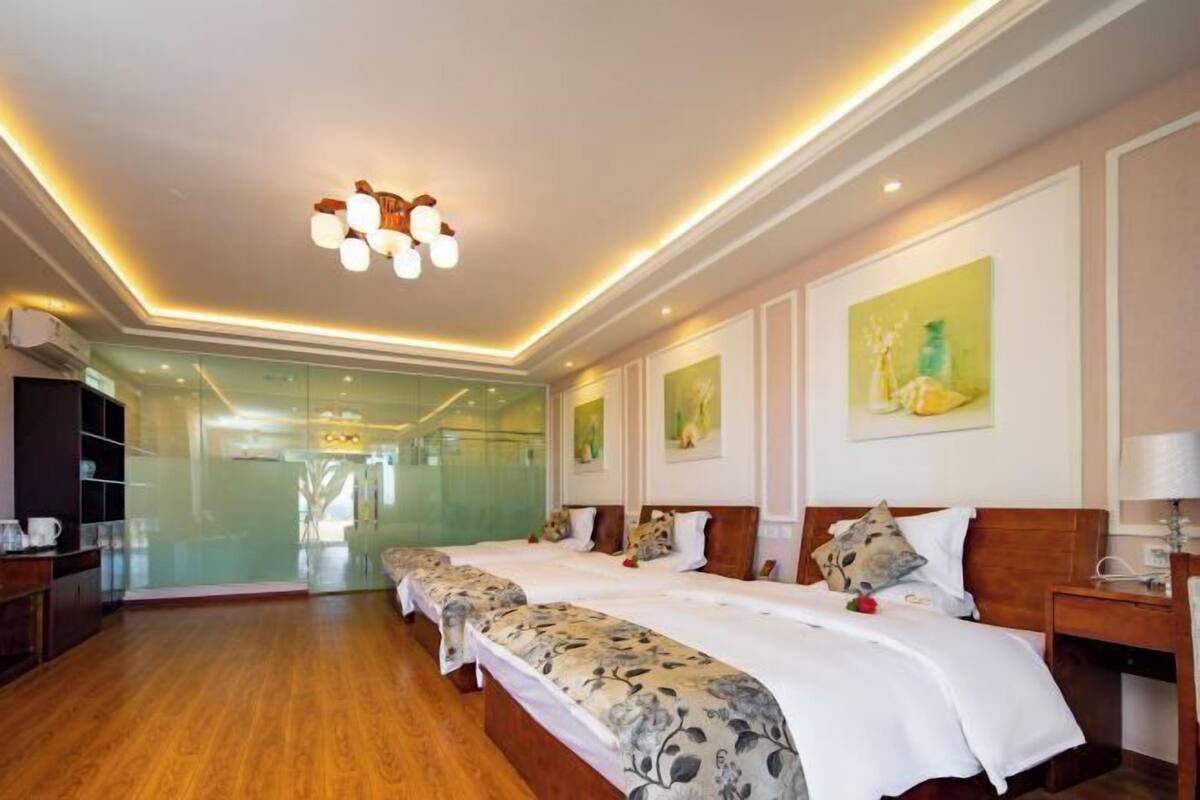 Habitación de hotel con una cama grande, un escritorio y una silla. Hay una pared de vidrio y una puerta que da a otra habitación.