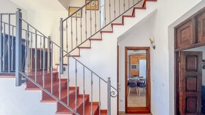 Una escalera con peldaños de madera y barandales metálicos, que conduce a una zona de cocina con armarios de madera y un refrigerador.