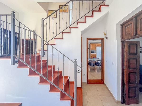 A staircase with wooden steps and metal railings, leading to a kitchen area with wooden cabinets and a refrigerator.