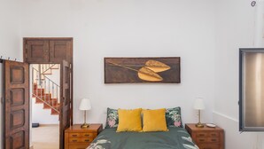 Un dormitorio con cama, dos mesitas de noche, una puerta de madera, una escalera y una obra de arte colgada en la pared.
