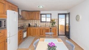 Una cocina compacta con armarios de madera, un refrigerador blanco y una zona de comedor con mesa y sillas.