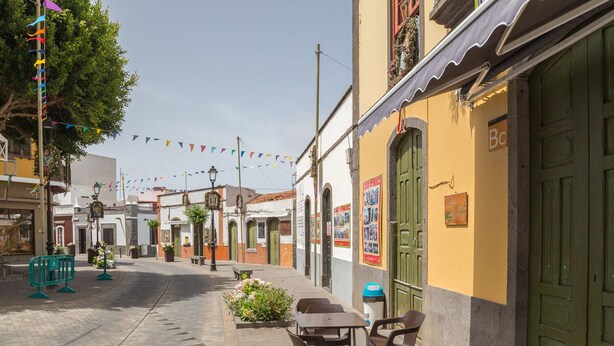 Una calle estrecha con edificios tradicionales, mesas al aire libre y decoraciones coloridas.