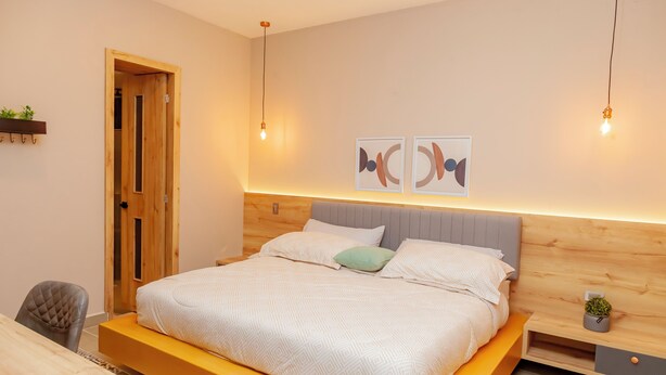 Un dormitorio moderno con estructura de cama de madera, una mesita de noche con una planta y un cuadro abstracto en la pared.