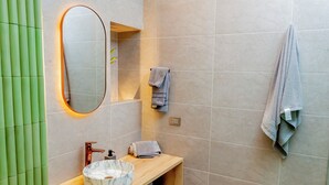 Un baño moderno con tocador de madera, lavabo de mármol, espejo con luz y un perchero para toallas.