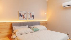 Un dormitorio moderno con cabecera de madera, una cama grande con ropa de cama estampada, dos obras de arte abstracto en la pared y una lámpara colgante.