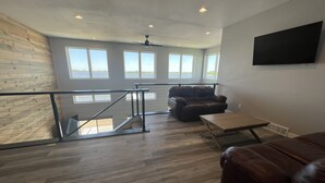 A spacious living area with a view of the outdoors, a brown leather sofa, a wooden coffee table, and a ceiling fan.