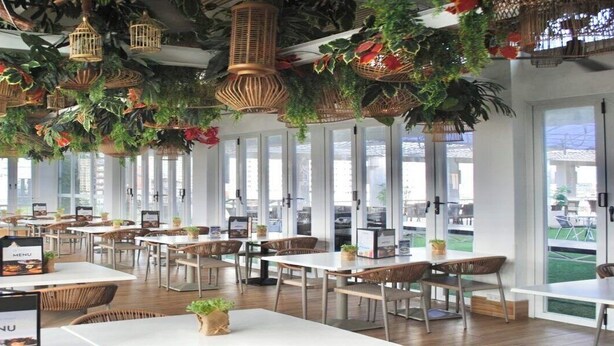 A restaurant with tables and chairs, hanging plants, and birdcages. - Selah Lofts Pasay (Pasay)