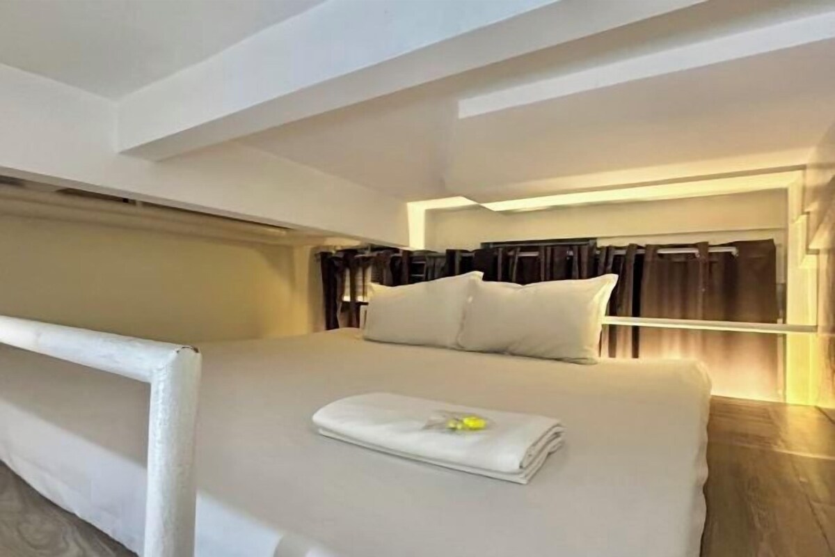 A modern hotel room with a large bed, a headboard with curtains, and a bedside table.