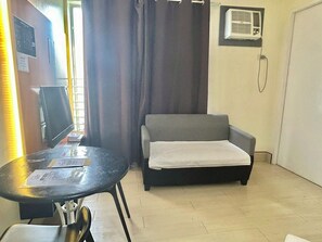 A room with a sofa, a small table, an air conditioning unit, and a window with curtains. - Selah Lofts Pasay (Pasay)