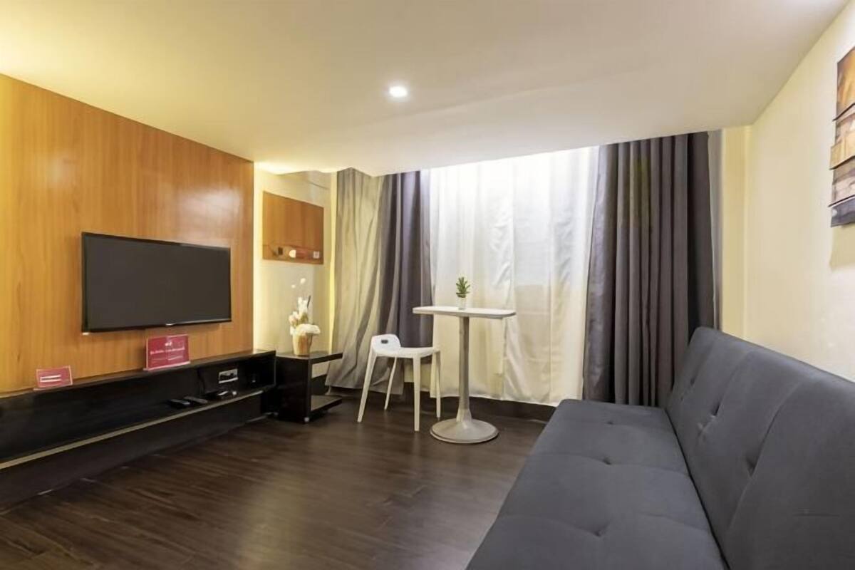 A modern living room with a flat-screen TV, a sofa, a small table, and a chair.