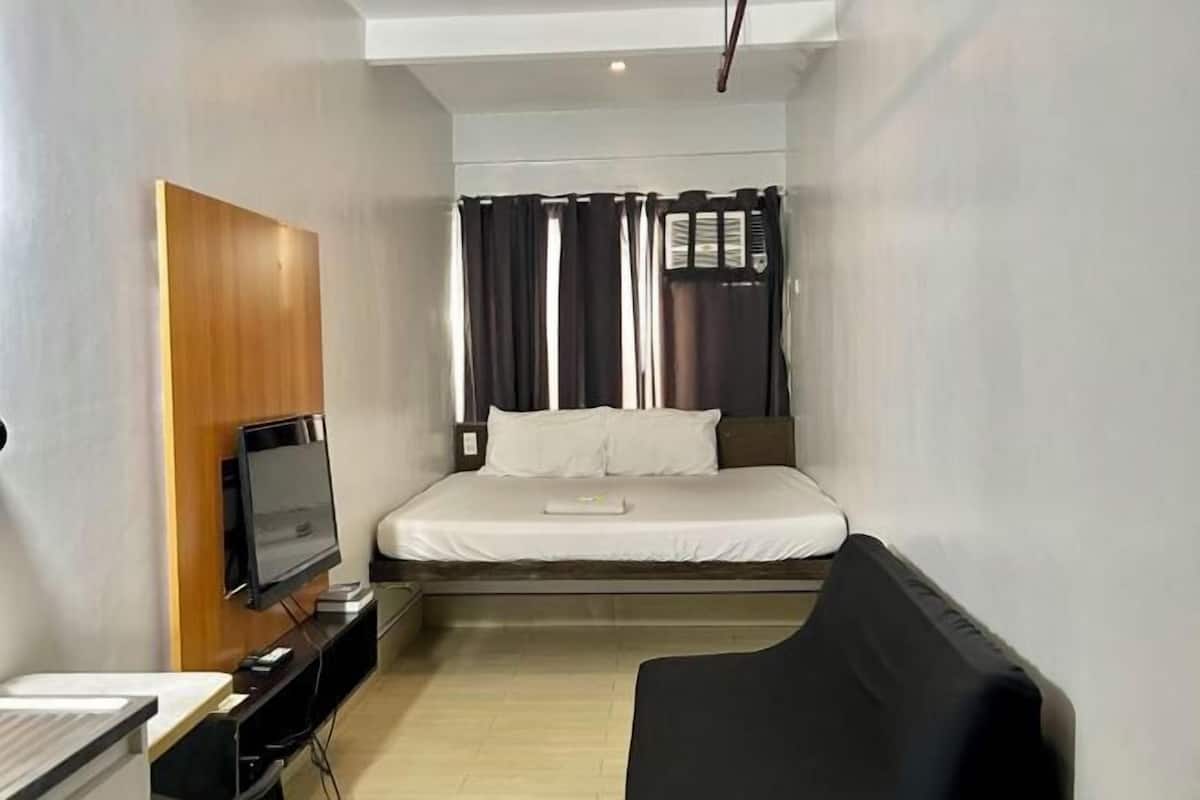 A compact hotel room with a bed, a television, a small desk, and a black sofa.