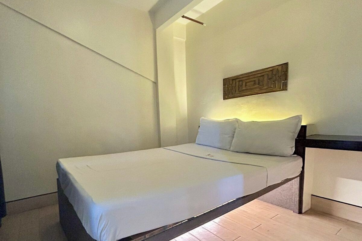 A single bed with a wooden frame and white bedding in a room with light wooden flooring and white walls.