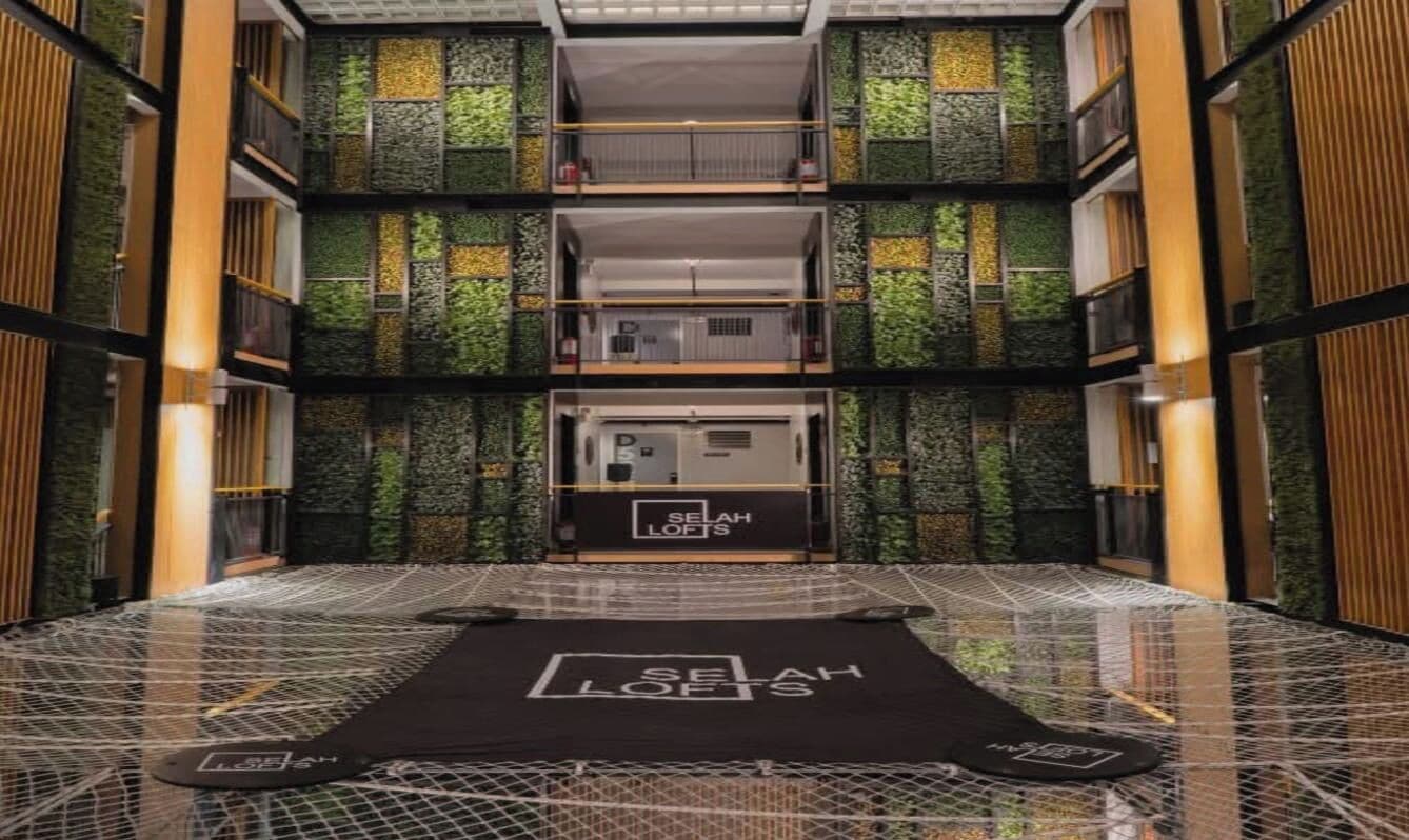 A hotel interior with a central elevator, a patterned floor, and a green wall with vertical elements.