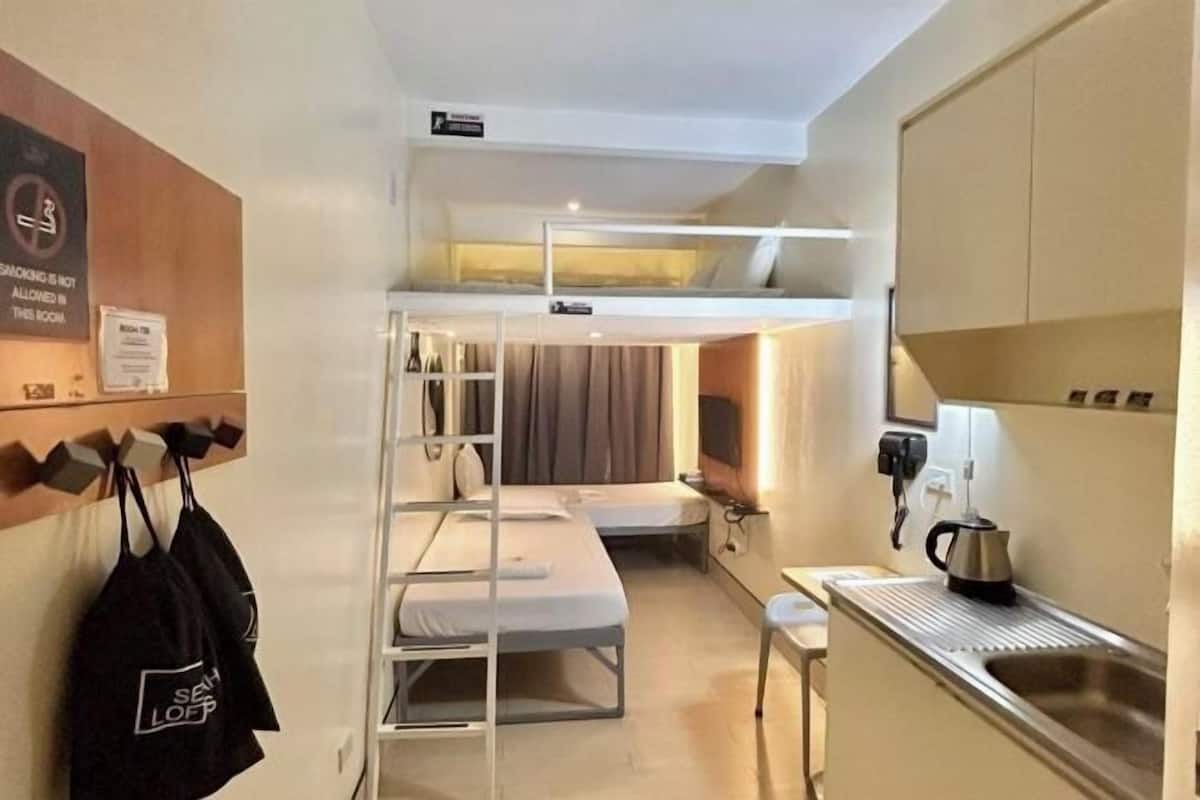 A compact room with bunk beds, a small kitchenette, and a wall-mounted shelf with bags.