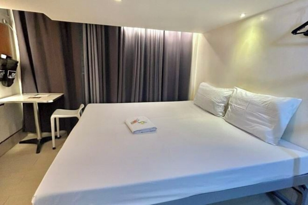 A hotel room with a bed, a small table, a chair, and a coat rack.