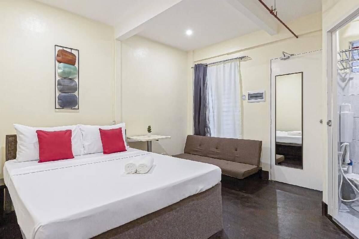 A hotel room with a bed, a sofa, a small table, and a shower area.