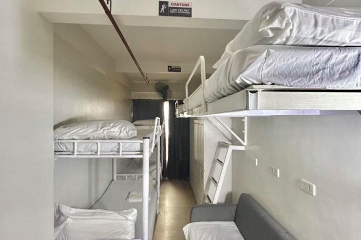 A narrow corridor with bunk beds on either side, a small seating area, and a caution sign on the wall.