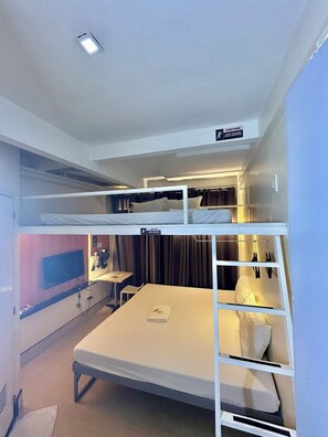 Une chambre avec un lit superposé, une télévision, un bureau et un panneau d’avertissement indiquant une faible hauteur sous plafond.