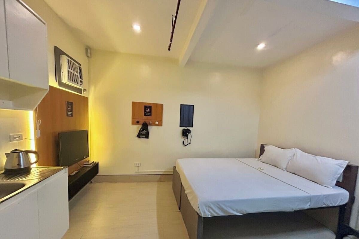 A hotel room with a bed, a television, a kettle, a wall-mounted heater, and a phone.