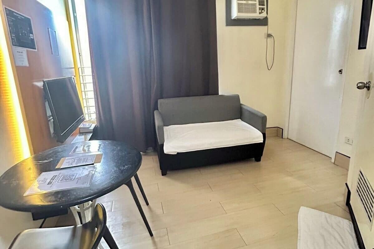 A small, well-lit room with a sofa, a table with chairs, a television, and a door.
