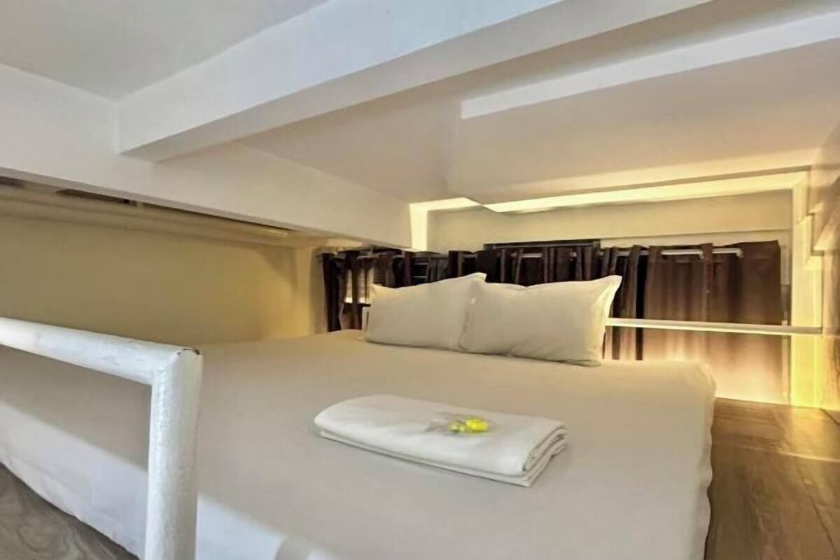 A modern hotel room with a large bed, a headboard with curtains, and a bedside table.