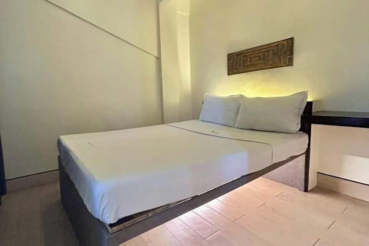 A single bed with a white mattress and pillows, a bedside table, and a wall-mounted artwork.