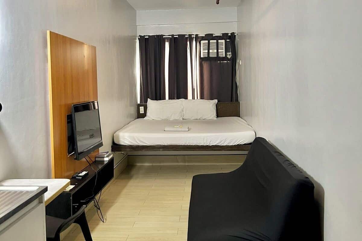 A compact hotel room with a bed, a TV, a desk, and a black couch.