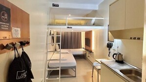 A compact hotel room with bunk beds, a kitchenette, a small table, and a wall-mounted shelf with bags. - Selah Lofts Pasay (Pasay)