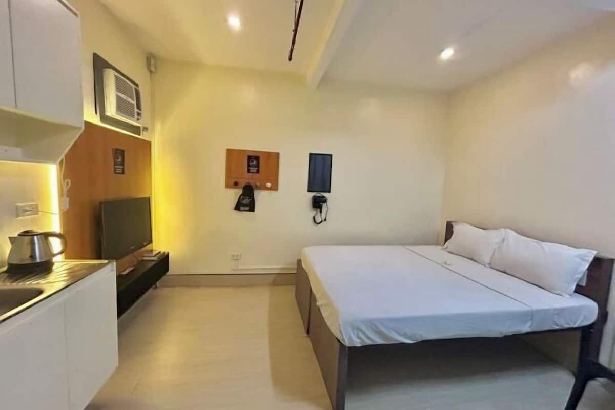 A small, modern room with a bed, a TV, a kettle, and a phone on the wall.