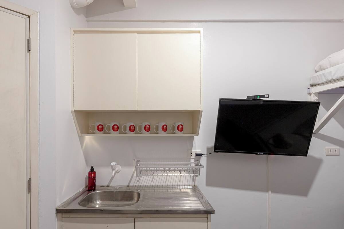 A small kitchenette with a sink, a microwave, and a shelf with six mugs.