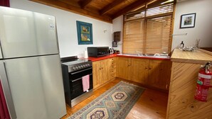A compact kitchen with a refrigerator, stove, microwave, and wooden cabinets. - Currawong Cottage - Fishing Paradise (Anglers Reach)