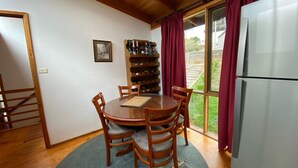 A dining area with a wooden table and chairs, a wine rack with bottles, and a refrigerator. - Currawong Cottage - Fishing Paradise (Anglers Reach)