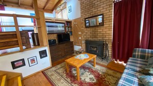 A cozy living room with a fireplace, wooden furniture, and a television. - Currawong Cottage - Fishing Paradise (Anglers Reach)