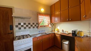 Cocina compacta con estufa a gas, un lavamanos, armarios de madera y una ventana con cortinas.