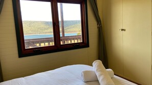 Un dormitorio con un amplio ventanal que ofrece vistas panorámicas de un bosque y una masa de agua.