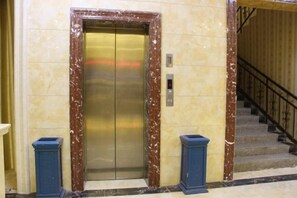 Ein Aufzug mit Marmorrahmen, Bedienfeld und einer Treppe mit Handlauf.