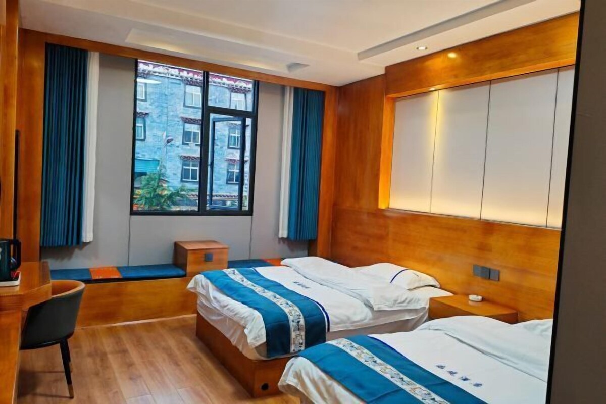 Quarto de hotel com duas camas, uma mesa, uma cadeira e janela com vista para edifícios.