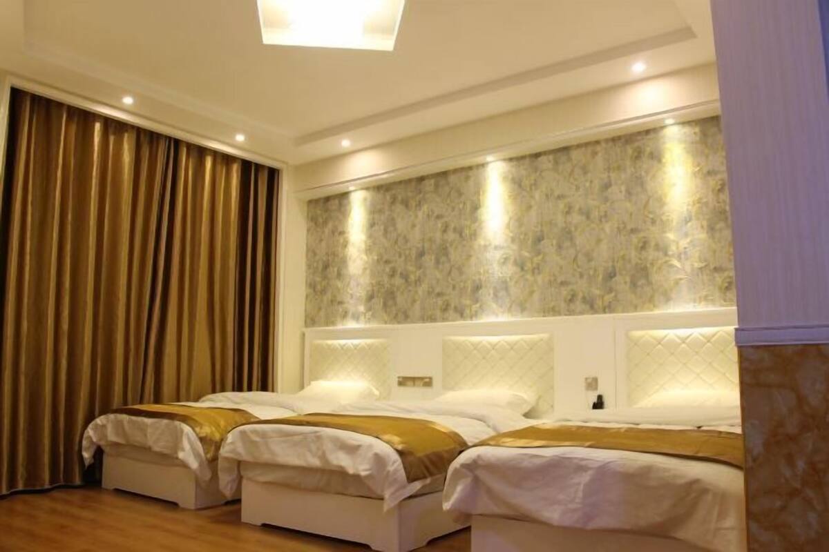 A hotel room with three beds, a large window with curtains, and a patterned wall.