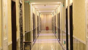 Un largo pasillo de hotel, estrecho, con puertas a ambos lados, un suelo brillante y un objeto rojo a lo lejos.