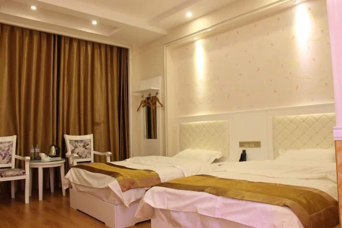 A hotel room with two beds, a small table, two chairs, and a large window with curtains.