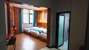 Habitación de hotel con escritorio, dos camas, zona de ducha y vistas al exterior.