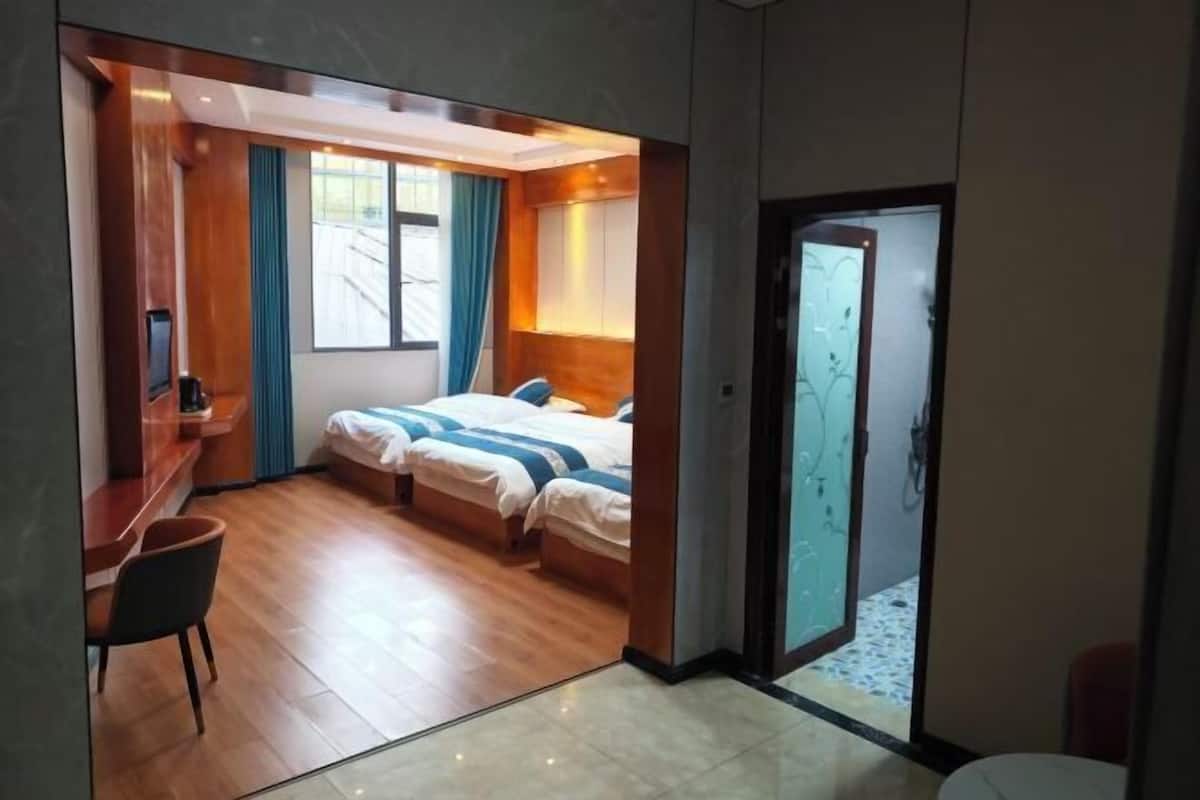 A hotel room with a desk, two beds, a shower area, and a view of the outdoors.
