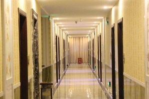 A long, narrow hotel corridor with doors on both sides, a polished floor, and a red object on the right. - Dongri Yanguang Hotel (Shangri-La)