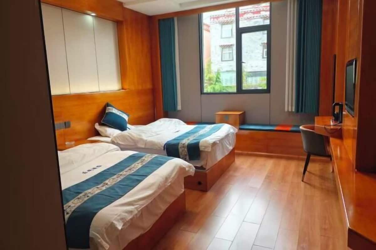 A hotel room with two beds, a desk, a chair, a TV, and a window with curtains.