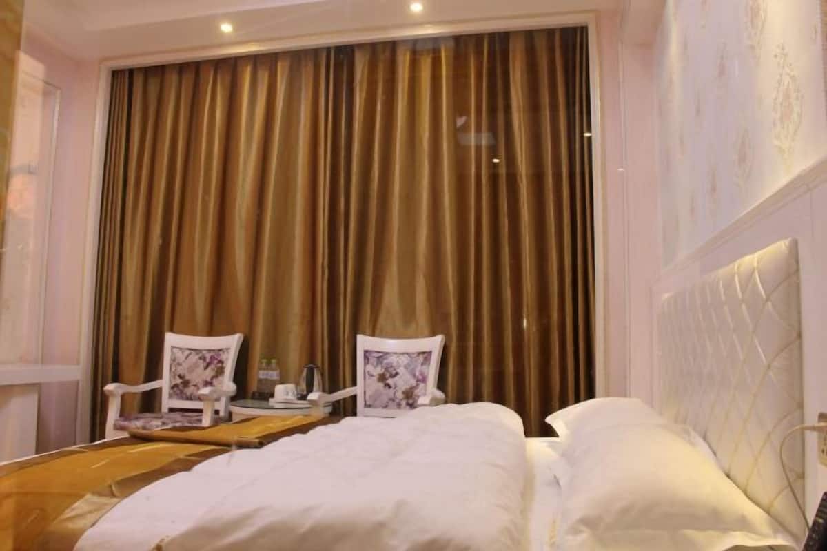 A hotel room with a large bed, two chairs, a small table, and a curtain.