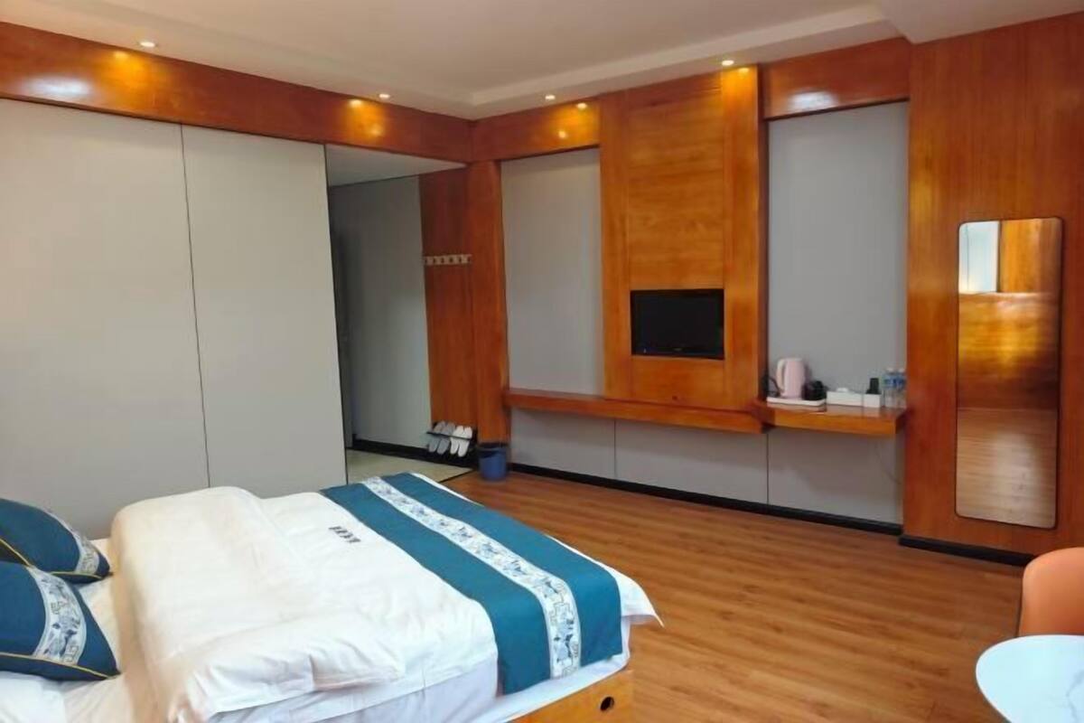 A hotel room with a bed, a TV, a mirror, and a wooden floor.